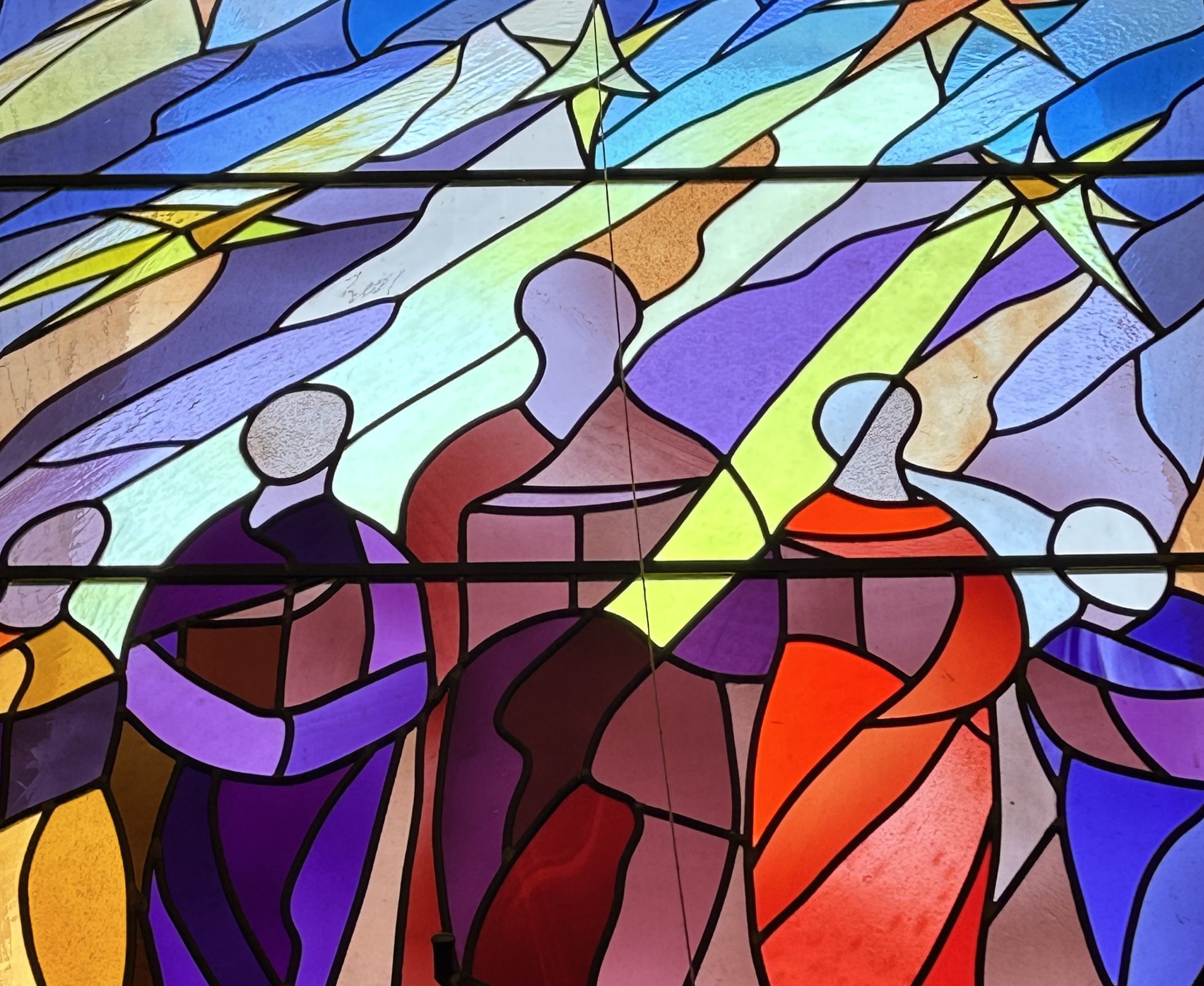 Stained glass window at Christ Church Uniting, Wayville. Five people dressed in yellow, purple, maroon, red, blue, with a purple and yellow background